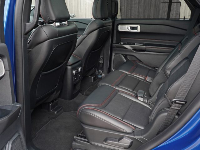 Binnenaanzicht van een Ford Explorer PHEV met de achterbank en deur, bekleed met zwart leer met rode stiksels.