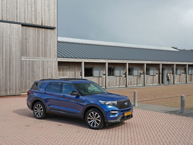 Een blauwe Ford Explorer PHEV geparkeerd voor een modern gebouw met houten lambrisering en een metalen dak.