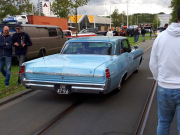 Een vintage lichtblauwe auto geparkeerd tijdens de Saturday Night Cruise 2020, terwijl omstanders toekijken.