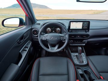 Binnenaanzicht van een Hyundai Kona met het stuur, het dashboard en de digitale displays, met uitzicht op een landingsbaan buiten.