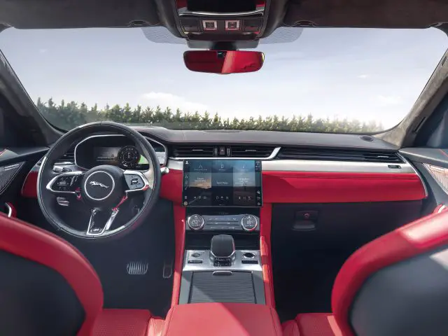 Binnenaanzicht van een Jaguar F-Pace met een strak dashboard, voorzien van een stuur, digitale displays en roodleren stoelen.