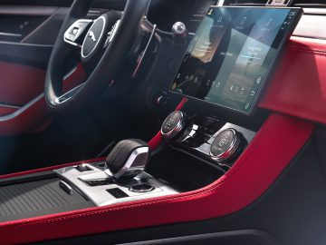 Binnenaanzicht van een moderne Jaguar F-Pace met een rood en zwart dashboard met een groot touchscreen-display en een versnellingspook.