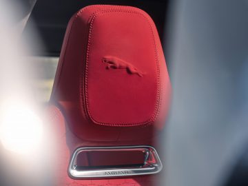 Close-up van een rode hoofdsteun van een Jaguar F-Pace-autostoel met een logo in reliëf van een springende jaguar en een naamplaatje.