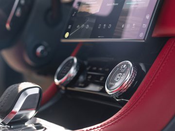Luxe Jaguar F-Pace-interieur met de nadruk op digitaal display, analoge klok en versnellingspook, met rood lederen stoelen.