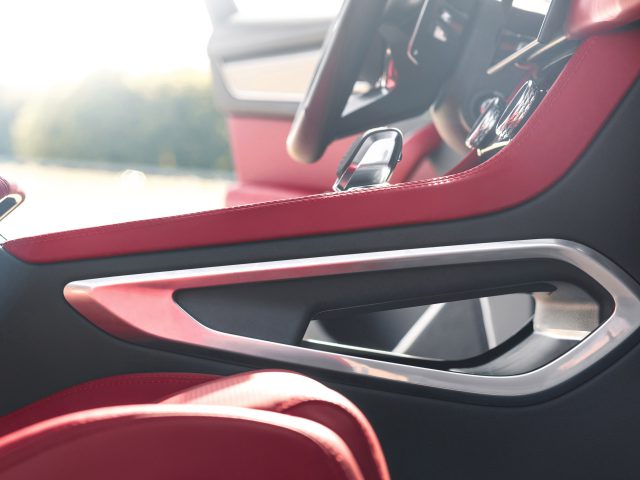 Binnenaanzicht van een Jaguar F-Pace met roodleren deurbekleding, zilveren deurgreep en een glimp van het stuur en het dashboard.