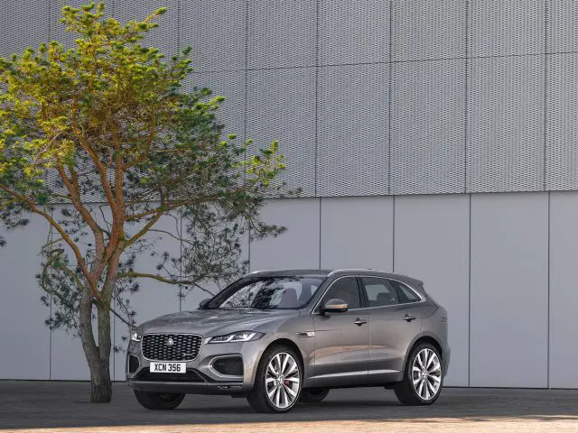 Een zilveren Jaguar F-Pace luxe SUV geparkeerd naast een boom tegen een moderne grijze muur.