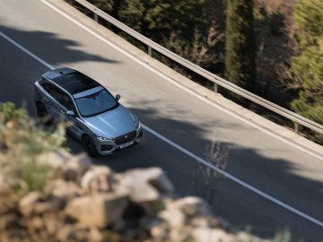 Een zilveren Jaguar F-Pace die op een bochtige weg door een bosrijk gebied rijdt, vastgelegd vanuit een verhoogde hoek met een wazige voorgrond.