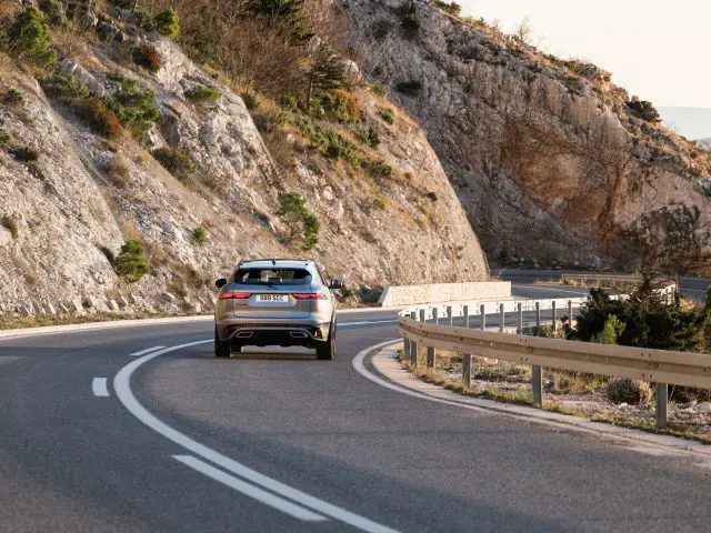 Een Jaguar F-Pace die bij zonsondergang over een bochtige weg door rotsachtige heuvels rijdt.