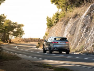 Een zilveren Jaguar F-Pace SUV die over een bochtige weg rijdt, omzoomd met zonovergoten rotsformaties en bomen.