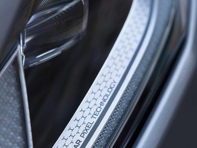 Close-up van het koplampdetail van een Jaguar F-Pace met een label met de tekst "Jaguar Pyrotechnology" op een gestructureerde metalen rand.