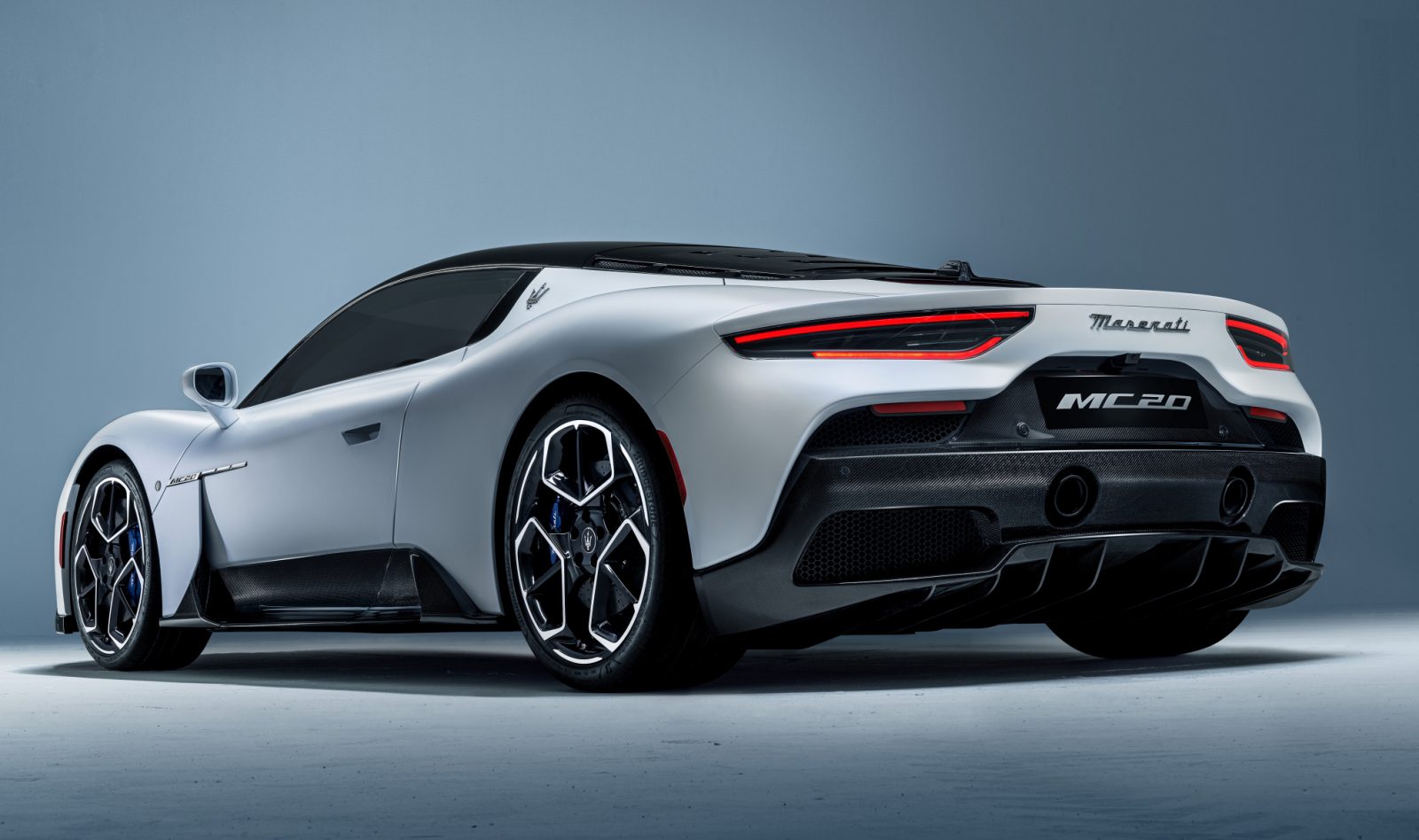 Een zilveren Maserati MC20-sportwagen, gezien vanaf de achterkant tegen een grijze achtergrond.