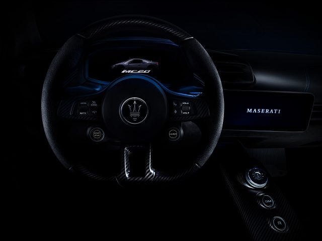 Binnenaanzicht van een Maserati MC20-auto, gericht op het stuur en het dashboard met verlichte bedieningselementen en merklogo.