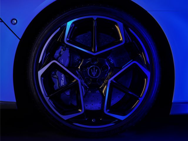 Close-up van een Maserati MC20-autowiel met een gedetailleerd velgontwerp en zichtbare remklauw, verlicht door blauw licht.