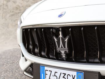 Close-up van de grille en het embleem van een witte Maserati Quattroporte-auto met een zichtbare Europese kentekenplaat.