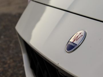 Close-up van een Maserati Quattroporte-embleem op de motorkap van een witte auto.