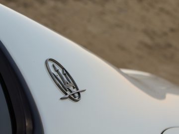 Close-up van een zilveren Maserati Quattroporte-logo-embleem op de achterkant van een witte auto, met een onscherpe achtergrond.