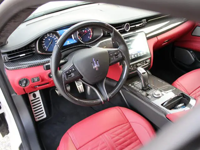 Binnenaanzicht van een Maserati Quattroporte met een stuur met logo, roodleren stoelen en een gedetailleerd dashboard met digitale displays.