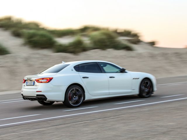 Maserati Quattroporte rijdt te hard op een kustweg met bewegingsonscherpteachtergrond.