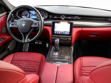 Interieur van een Maserati Quattroporte met roodleren stoelen, een centraal touchscreen en een dashboard van koolstofvezel.