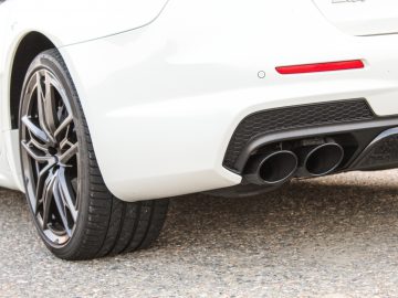 Close-up van het achterwiel en het uitlaatsysteem van een witte Maserati Quattroporte, waarbij het gedetailleerde ontwerp en de structuur zichtbaar zijn.