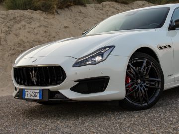 Een witte Maserati Quattroporte geparkeerd op een zandvlakte, met een gedetailleerde weergave van de grille en het embleem aan de voorkant, met de nadruk op het strakke ontwerp en de sportieve wielen.