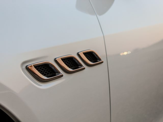 Close-up van drie rechthoekige ventilatieopeningen aan de zijkant van een witte Maserati Quattroporte, met een zachte focusachtergrond.