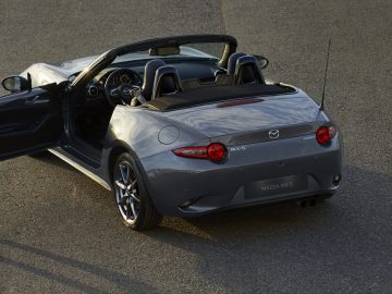 Een Mazda MX-5 Ginzan-cabriolet geparkeerd, met open dak en passagiersdeur op een kier, bij daglicht.