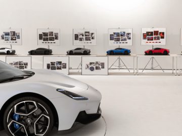 Een witte Maserati Grecale in een galerij met schetsen van autoconcepten en modelauto's op planken.