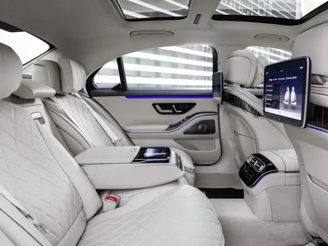 Binnenaanzicht van de achterbank van een Mercedes-Benz S-Klasse met leren stoelen, hightech bedieningspanelen en grote schermen.