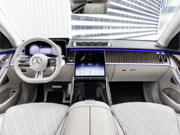 Interieur van een moderne Mercedes-Benz S-Klasse, met witleren stoelen, houten lambrisering en een prominent centraal touchscreen.