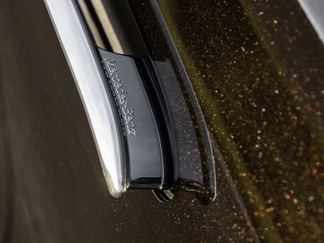 Close-up van een Mercedes-Benz S-Klasse-modelbadge op een sprankelend gouden voertuig.