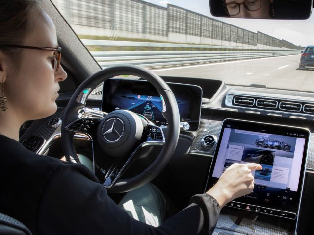 Vrouw met touchscreen-dashboard in een Mercedes-Benz S-Klasse op een snelweg.