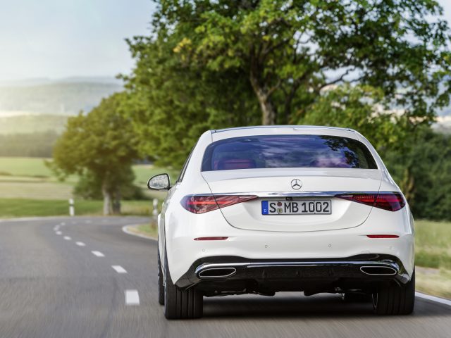 Witte Mercedes-Benz S-Klasse rijdt op een bochtige weg door een schilderachtig landschap.