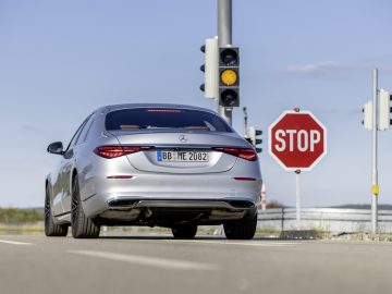 Een zilveren Mercedes-Benz S-Klasse sedan stopte op een zonnige dag voor een rood licht naast een stopbord.
