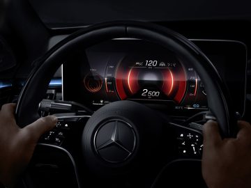 Bestuurdersaanzicht van een Mercedes-Benz S-Klasse stuur en digitaal dashboard dat de snelheid en het motortoerental weergeeft.