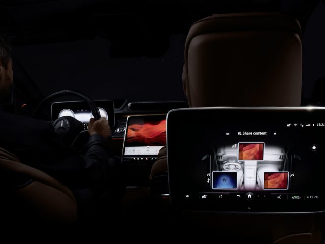 Een man die 's nachts in een Mercedes-Benz S-Klasse rijdt terwijl hij communiceert met geavanceerde digitale displays op het dashboard en het tabletscherm achterin.