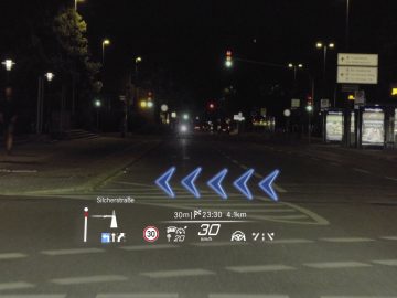 Head-up display (hud) in een Mercedes-Benz S-Klasse met navigatie- en snelheidsinformatie op een nachtelijk straatbeeld met verkeerslichten en voetgangers.