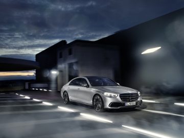 Luxe Mercedes-Benz S-Klasse die in de schemering door een stadsstraat rijdt, met dynamische verlichting en modern design.