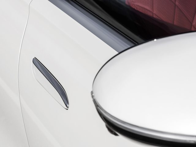 Close-up van de buitenkant van een witte Mercedes-Benz S-Klasse, met een deel van een glanzende deur en een ronde zijspiegel.