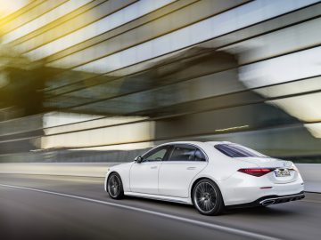Witte Mercedes-Benz S-Klasse sedan die langs een wazig modern gebouw op een snelweg snelt en beweging en snelheid overbrengt.