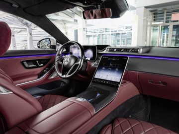 Binnenaanzicht van een Mercedes-Benz S-Klasse met bordeaux lederen stoelen, voorzien van een modern dashboard en een groot touchscreen-display.