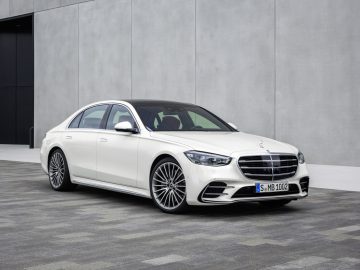 Witte Mercedes-Benz S-Klasse sedan geparkeerd voor een modern grijs gebouw met een eenvoudig, minimalistisch design.