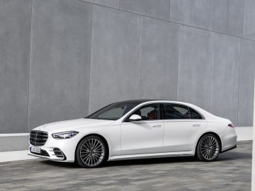 Een witte Mercedes-Benz S-Klasse geparkeerd voor een effen grijze muur, met een strak ontwerp en grote lichtmetalen velgen.