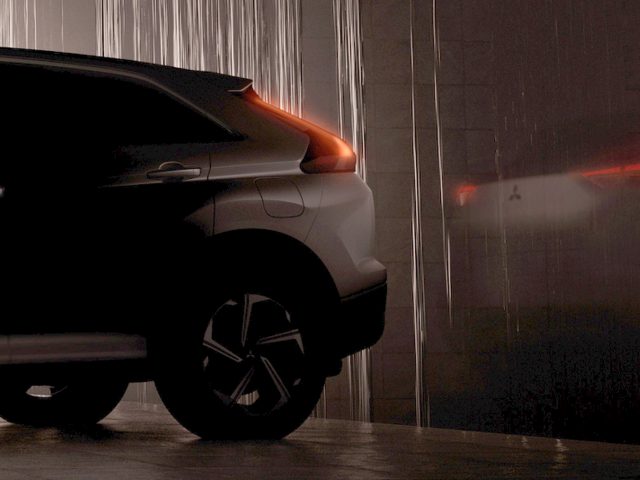 Een donkere Mitsubishi Eclipse Cross parkeerde 's nachts naast een regenachtig raam, terwijl de rode achterlichten van een andere auto zichtbaar waren in de weerspiegeling.