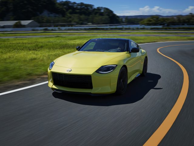 Een gele Nissan Z Proto rijdt op een bochtige weg met een schilderachtig landschap op de achtergrond.