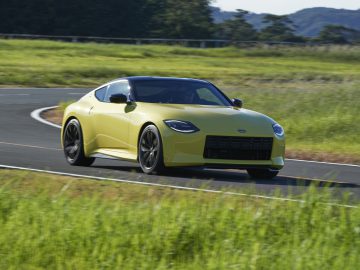 Een gele Nissan Z Proto-sportwagen die op een gebogen weg rijdt met groene velden en bomen op de achtergrond.