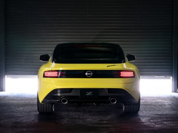 Achteraanzicht van een gele Nissan Z Proto-sportwagen geparkeerd voor een gedeeltelijk verhoogde garagedeur, verlicht door bovenlichten.