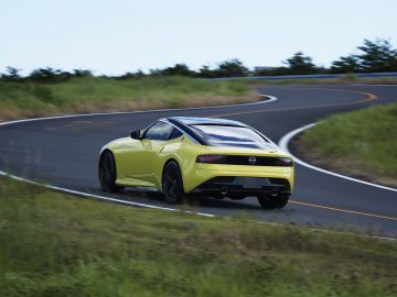 Een gele Nissan Z Proto snelt over een bochtige weg omringd door grasvelden.