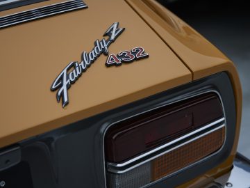 Close-up van het achterembleem en het achterlicht van een vintage Nissan Z Proto op een gouden carrosserie.