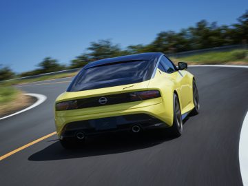 Een gele Nissan Z Proto snelt over een bochtige weg onder een helderblauwe lucht.